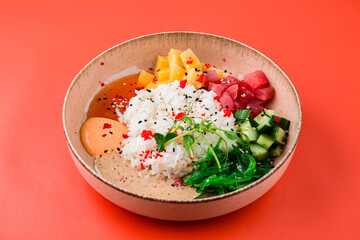 Asian food rice with raw tuna, mango, cucumber, seaweed, sesame and sauces on a red background.
