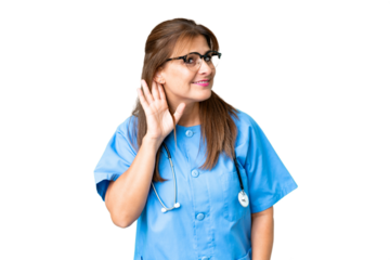 Middle age nurse woman over isolated background listening to something by putting hand on the ear