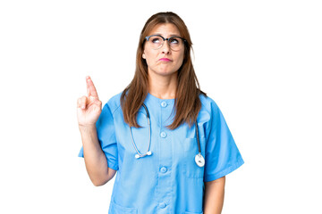 Middle age nurse woman over isolated background with fingers crossing and wishing the best