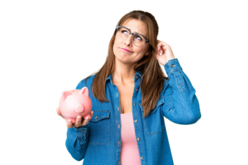 Middle age caucasian woman holding a piggybank over isolated background having doubts and with confuse face expression