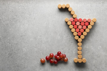 Cocktail glass with straw made of wine bottle corks and grapes on light grey table, flat lay. Space for text