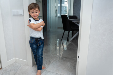 a small, cute, emotional boy is standing in the corridor, leaning against the wall, surprised, moving his hands, smiling. Close-up portrait view