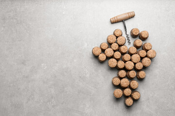 Grape made of wine bottle corks and corkscrew on light grey table, top view. Space for text