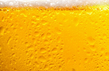 Glass of tasty cold beer with foam and condensation drops on white background, closeup
