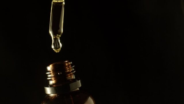 Slow motion macro close up of drops of dosage of organic and organic hemp herbal pharmaceutical cbd oil from container on black background.