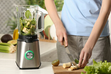 Woman preparing ingredients for tasty green smoothie at white wooden table in kitchen, closeup