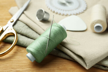Fototapeta na wymiar Spool of thread and sewing tools on wooden table, closeup