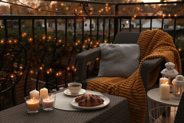 Beautiful view of garden furniture with pillow, soft blanket and burning candles at balcony