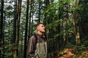 Portrait of a handsome young man in casual clothes standing on a path in the mountains and looking away with a serious face.