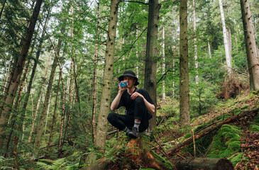 Funny young man tourist in panama during a hike sits in the forest in the mountains and drinks water and rests.