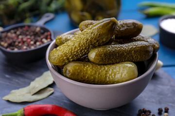 Bowl of pickled cucumbers and ingredients for food preservation on blue wooden table, closeup