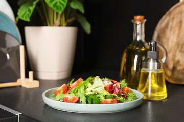 Plate of salad and bottles with cooking oil on black table in kitchen