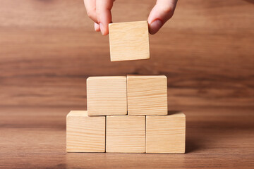 Woman building pyramid of cubes on wooden background, closeup with space for text. Idea concept