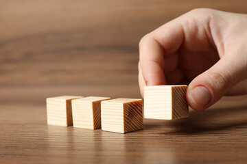 Woman arranging cubes on wooden background, closeup. Idea concept