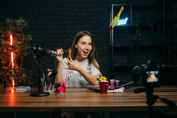 Emotional woman beauty blogger with cosmetics in hands talks to camera in studio and shakes tubes....