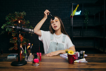 A beautiful young lady shows a make-up master class to the camera while sitting at the table and...