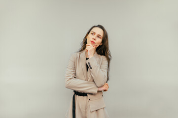 Portrait of a pensive female worker in a beige suit standing on a beige background, looking away and thinking. Copy space
