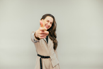 Joyful woman in a suit shows her fingers and looks at the camera with a joyful face on a beige...