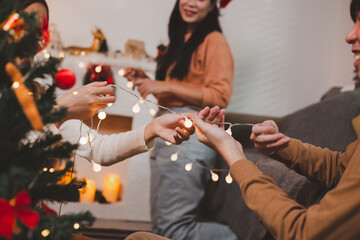 Group of happy Asian friends celebrating Christmas and decorate the Christmas tree indoors. Beauty woman with Christmas Gifts. New Year party. Woman hands decorate Christmas tree red ball, bauble.