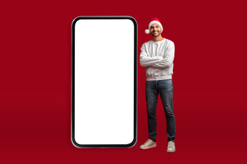 Online Offer. Handsome Arab Man In Santa Hat Posing Near Blank Smartphone