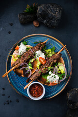 Kebab, barbecued beef on a stick with tomatoes, lettuce, onion, arugula, sour cream, tortilla and red sauce.