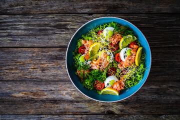 Salmon salad - smoked salmon, goat cheese and fresh vegetables on wooden table
