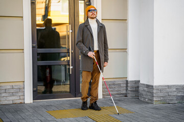 Blind man with a walking stick. Stands on a tactile tile for self-orientation while moving through...