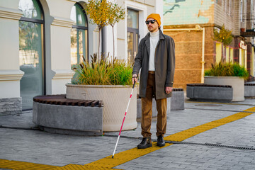 Blind man with a walking stick. Walks on tactile tiles for self-orientation while moving through...