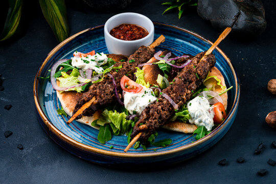 Hot kebab, barbecued beef on a stick with tomatoes, lettuce, onion, arugula, sour cream, tortilla and red sauce.