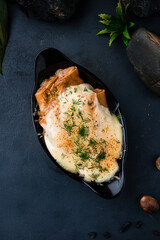 Thin pancakes with minced meat, onion and cheese sauce decorated with greens in a cast-iron bowl.