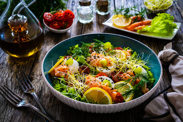 Salmon salad - smoked salmon, goat cheese and fresh vegetables on wooden table

