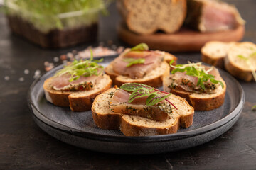 Bread sandwiches with jerky salted meat, sorrel and cilantro microgreen on black. side view, selective focus.