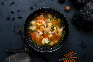 Chicken broth with potatoes, onions, tomatoes, carrots and herbs on a dark background.