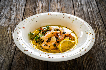 Roast prawns in butter sauce with lemon, garlic and parsley on wooden table
