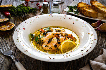 Roast prawns in butter sauce with lemon, garlic and parsley on wooden table
