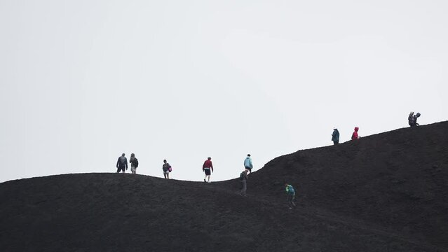 Tourists hiking through volcanic Mount Etna. People enjoying adventurous vacation at famous place. View of dramatic landscape with sky covered in smoke in background. Climbing mount Etna.