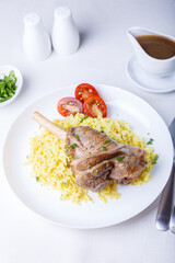 Lamb shin (shank) with rice, parsley, tomatoes and sauce on a white plate. Traditional dish. Close-up, selective focus.
