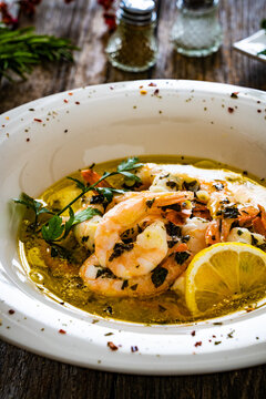 Roast prawns in butter sauce with lemon, garlic and parsley on wooden table

