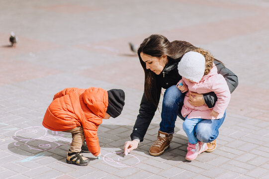 Little boy and girl, preschool child, friends and mother draw on the pavement, tiles in the city with multi-colored chalk. Photography, childhood.