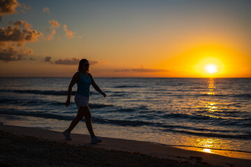 Fototapeta premium Woman walking on sunny, tropical beach at daybreak 