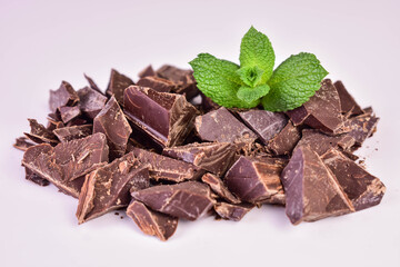 Pieces of dark chocolate on a white background with a mint leaf.
