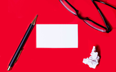 The business card lies on a bright red background next to a pen and glasses. Business concept.
