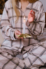 A girl holds a lit candle in her hands in a Christmas apartment. Candle close-up. Relaxation and zen atmosphere