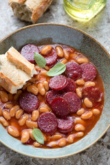 Close-up of stew with roasted chorizo sausage and white beans in a rustic plate, vertical shot, selective focus