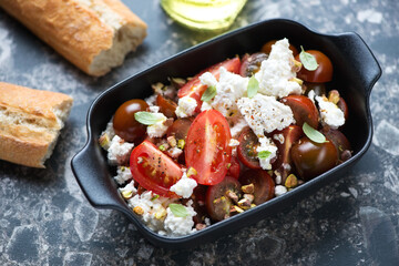 Salad with red tomatoes, ricotta cheese and pistachios in a black serving pan, middle close-up, horizontal shot
