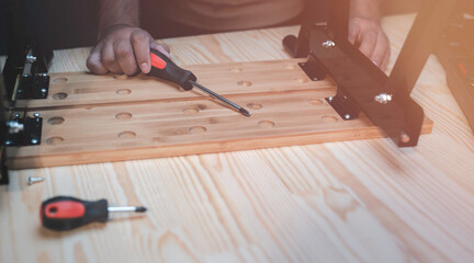 Man's hand using Phillips screwdriver to fasten screws in assembling wooden furniture in house
