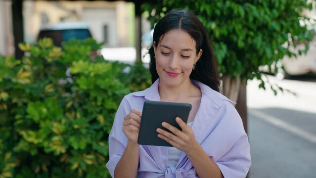 Young beautiful hispanic woman smiling confident using touchpad at street