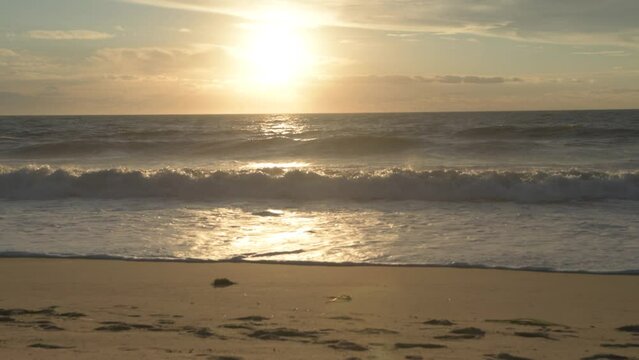 Bright sun shining over the sea waves crashing into sandy Bethany Beach during sunrise