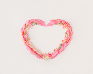 Heart-shaped frame made with pink petals and twigs with green leaves on an isolated pastel beige background. Minimal flat lay. Floral love symbol. Wedding or valentines day card. Blooming concept.
