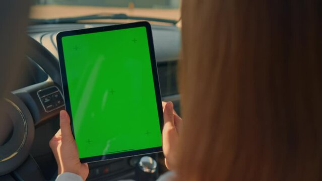 close up details woman in a car holding digital tablet tapping on green screen driver at the parking